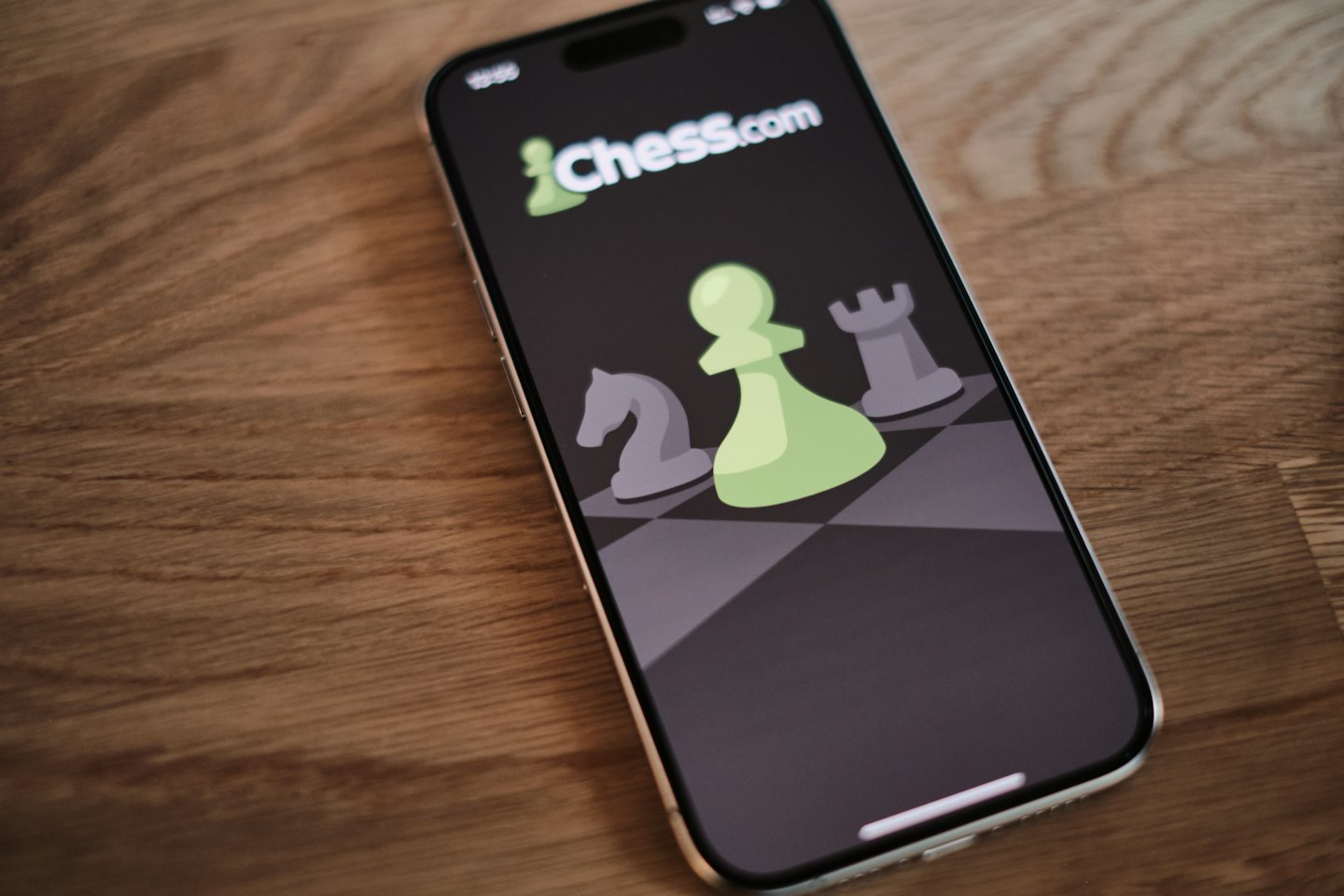 A smartphone screen displays chess pieces on a wooden table.