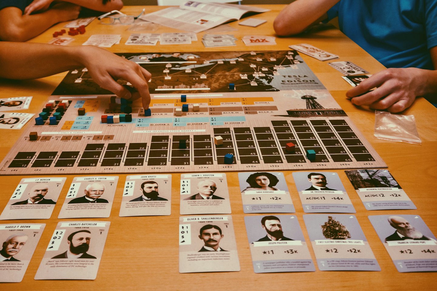 People's hands moving pieces on a detailed board game.