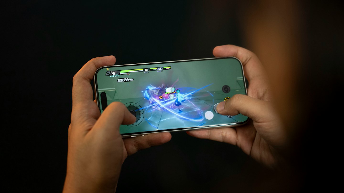 Hands holding a smartphone while playing an action mobile game.