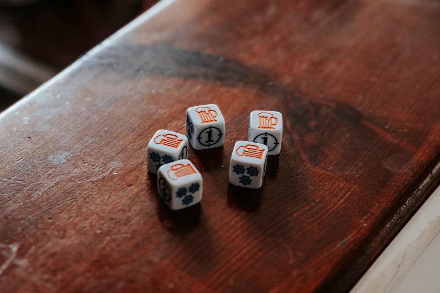 Five game dice with custom symbols scattered on a wooden table.